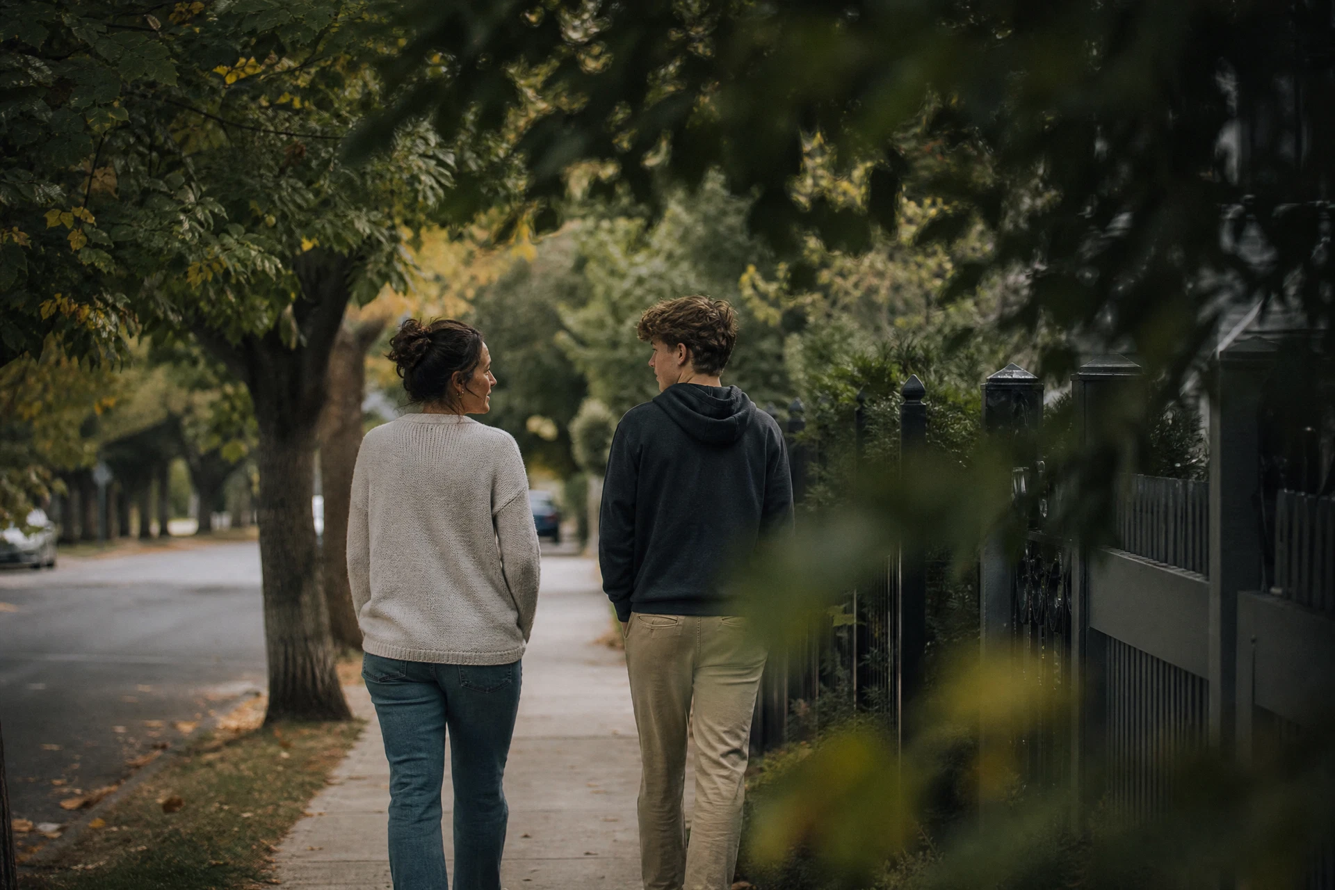 A parent and teenager walking side by side in a quiet neighborhood